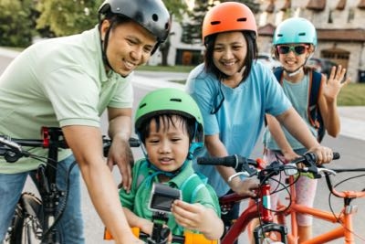 A family of four riding bicycles together on a sunny day, enjoying time outdoors in a park setting.